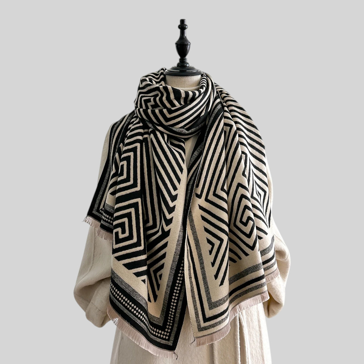 A black and cream geometric patterned scarf draped on a cream-colored dress form mannequin against a solid light gray background.