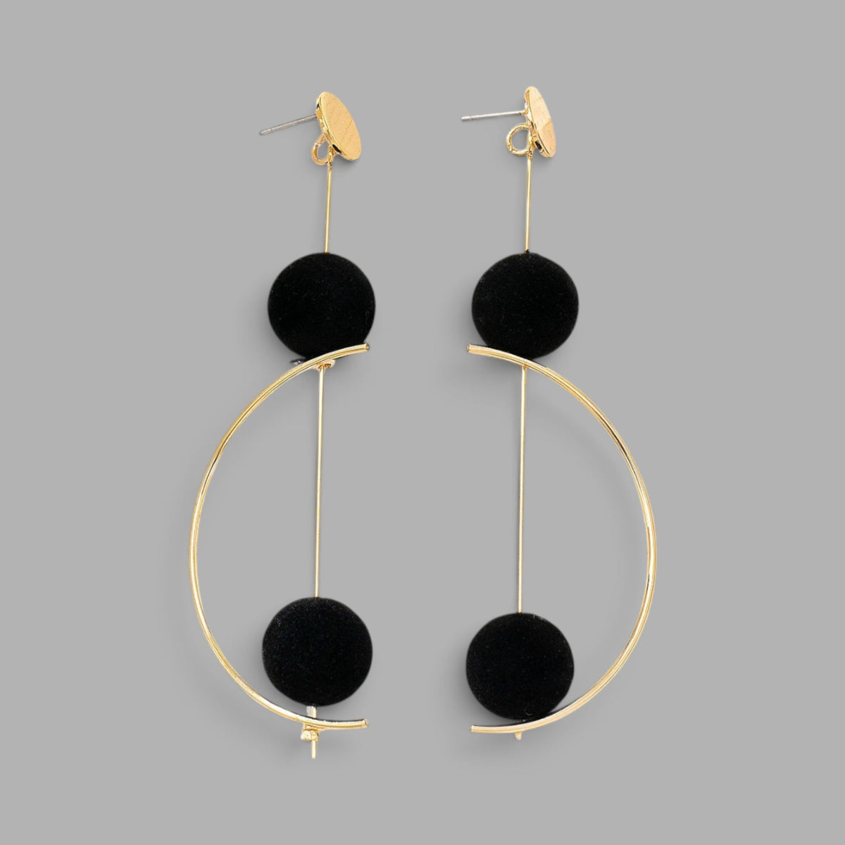 A pair of gold-tone statement dangle earrings featuring a large open circular hoop, a vertical bar, a black velvet sphere, and a small gold heart-shaped drop, shown against a solid gray background.