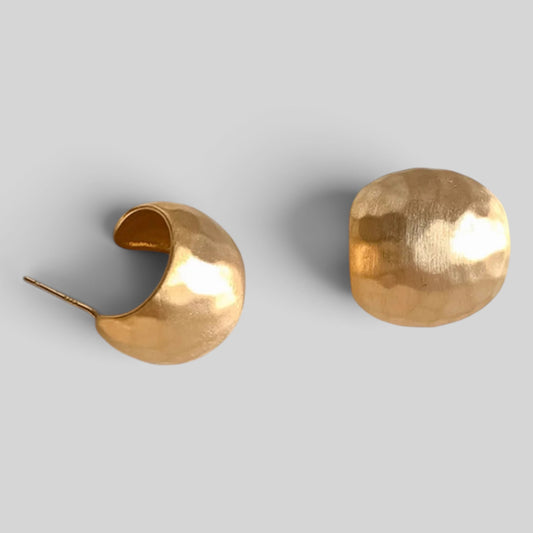 A pair of hammered gold crescent-shaped hoop earrings on a light gray background.