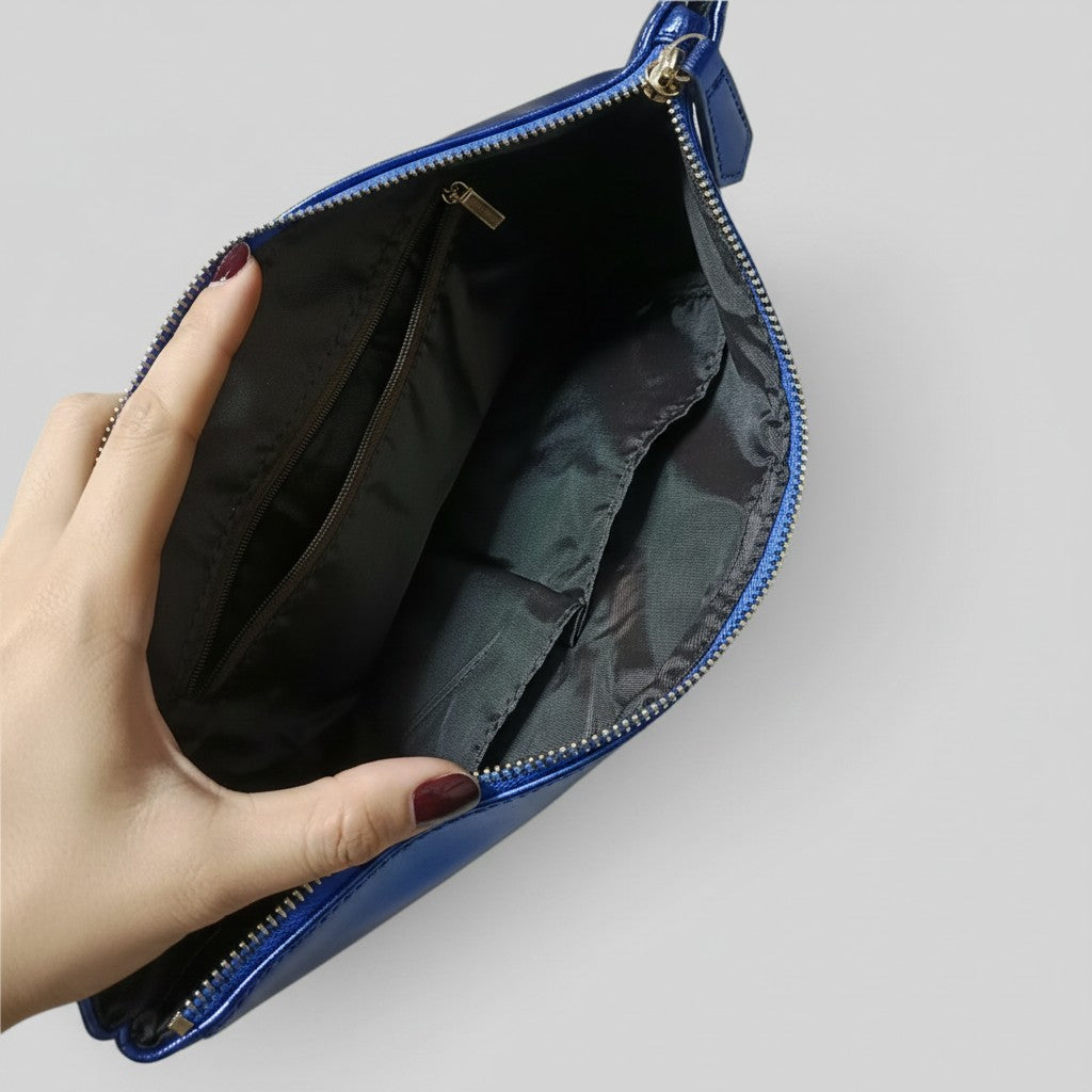 A close-up of a blue leather clutch or pouch shown open, held by a hand with dark red nail polish against a light gray background.