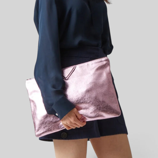 A person wearing a navy blue long-sleeve top and shorts holds a metallic rose gold clutch bag against a plain light gray background.