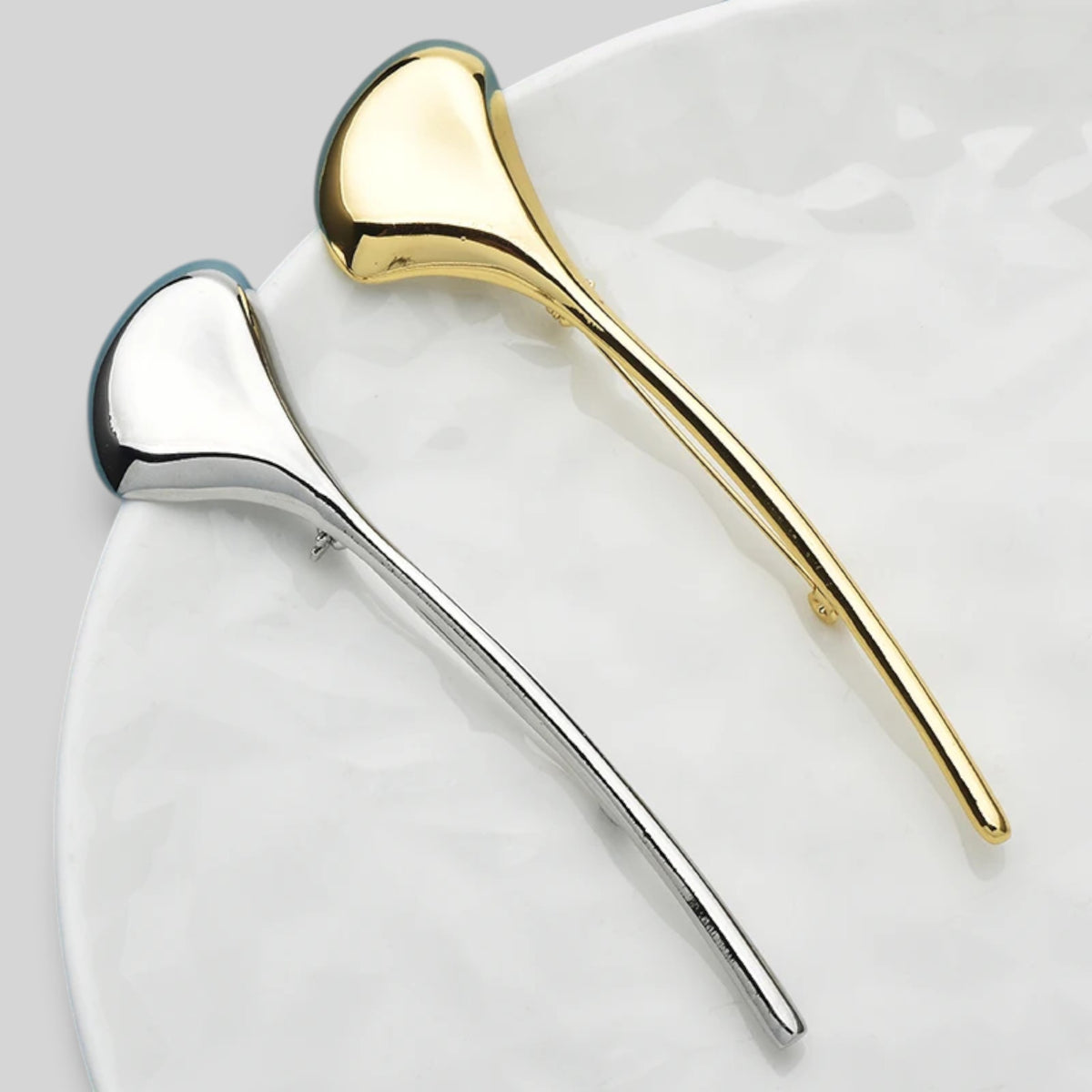 Two elegant hair claw clips in polished silver and gold finishes, displayed on a white marble-patterned plate.