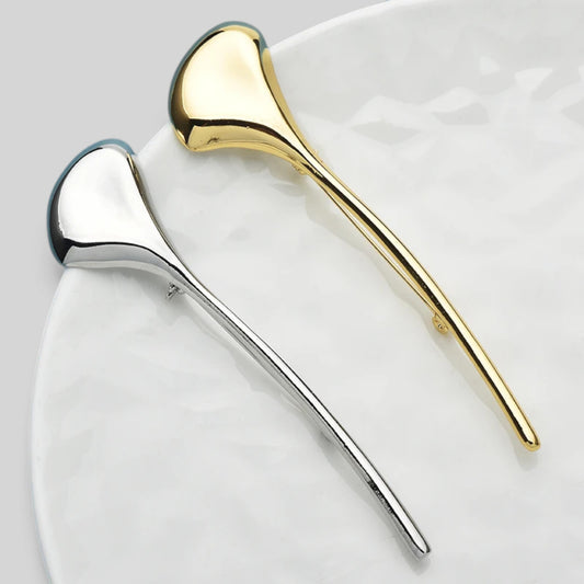 Two elegant hair claw clips in polished silver and gold finishes, displayed on a white marble-patterned plate.