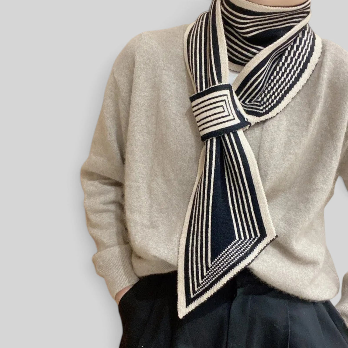 A close-up of a person wearing a cream knit sweater and a navy-and-cream striped scarf tied around the neck.