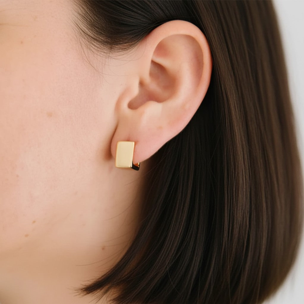 A close-up of a person's ear wearing a small rectangular gold stud earring.