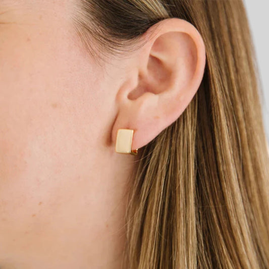 A close-up of a woman's ear wearing a small rectangular gold stud earring.