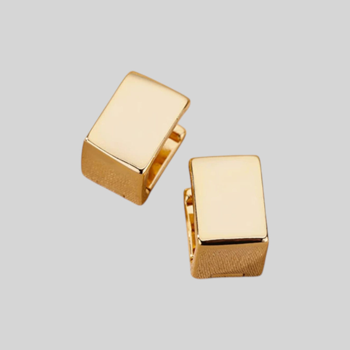A pair of gold-toned rectangular stud earrings with a smooth polished top surface and a textured side edge, shown on a solid light gray background.