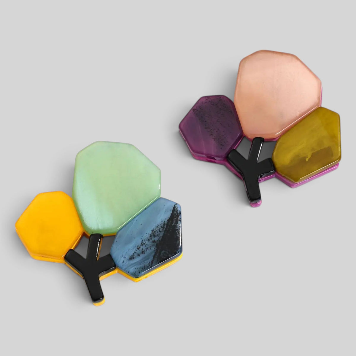 Two pairs of colorful geometric resin earrings on a light gray background. Each earring features five faceted, tree-like shapes in yellow, mint green, light blue, purple, and peach, connected by black Y-shaped links.