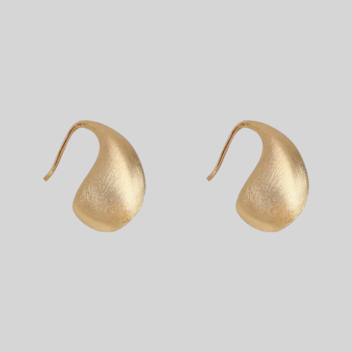 A pair of organic-shaped gold earrings with a textured, matte finish and curved hooks, shown on a solid light gray background.