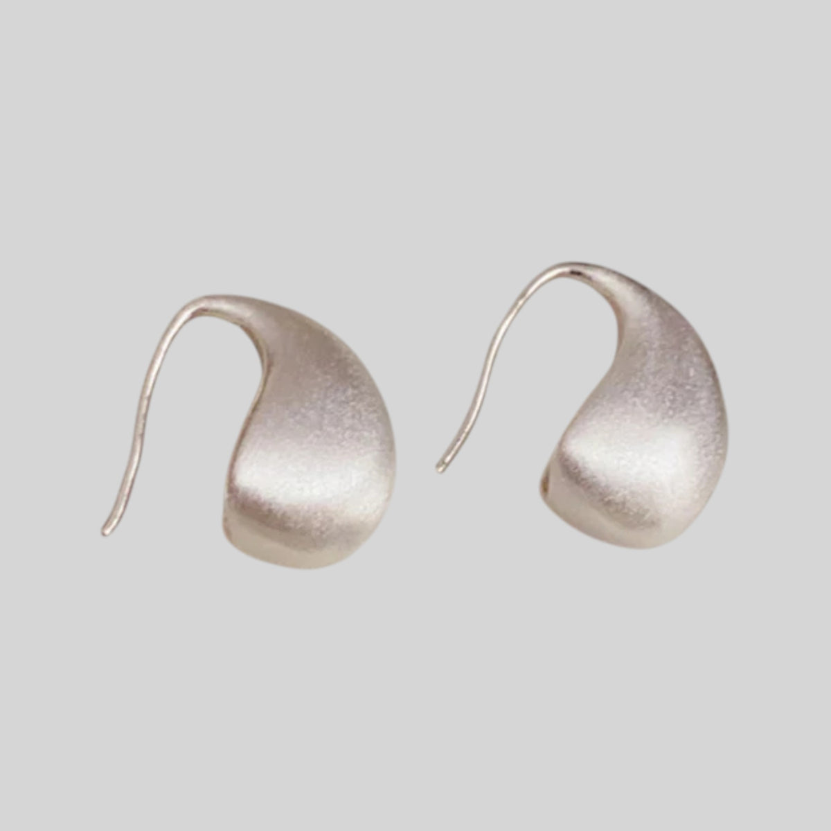 A pair of organic-shaped, teardrop-shaped stud earrings with a textured, matte metallic finish, shown on a solid light gray background.