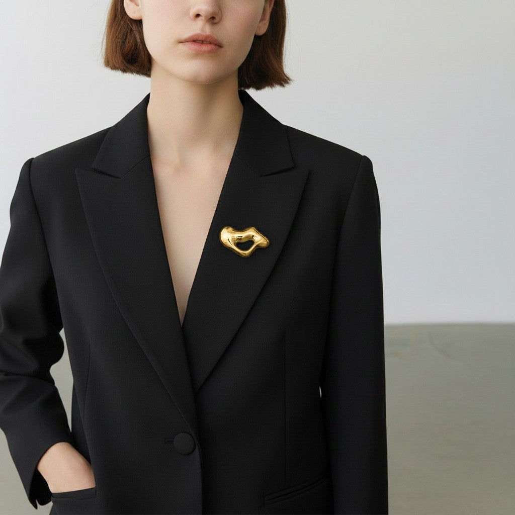 Model wearing gold circular wave brooch as an architectural accent on a Black blazer