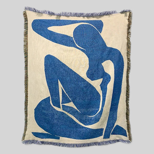 A square woven throw blanket featuring a large blue abstract human silhouette on an off-white background, with fringed edges, shown against a light gray studio background.