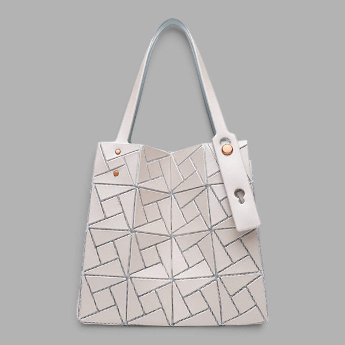 A structured tote bag with a geometric, faceted surface design in off-white and light gray, featuring dual shoulder straps and a hanging key ring detail, set against a solid gray background.