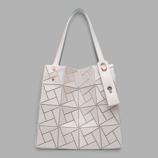 A structured tote bag with a geometric, faceted surface design in off-white and light gray, featuring dual shoulder straps and a hanging key ring detail, set against a solid gray background.
