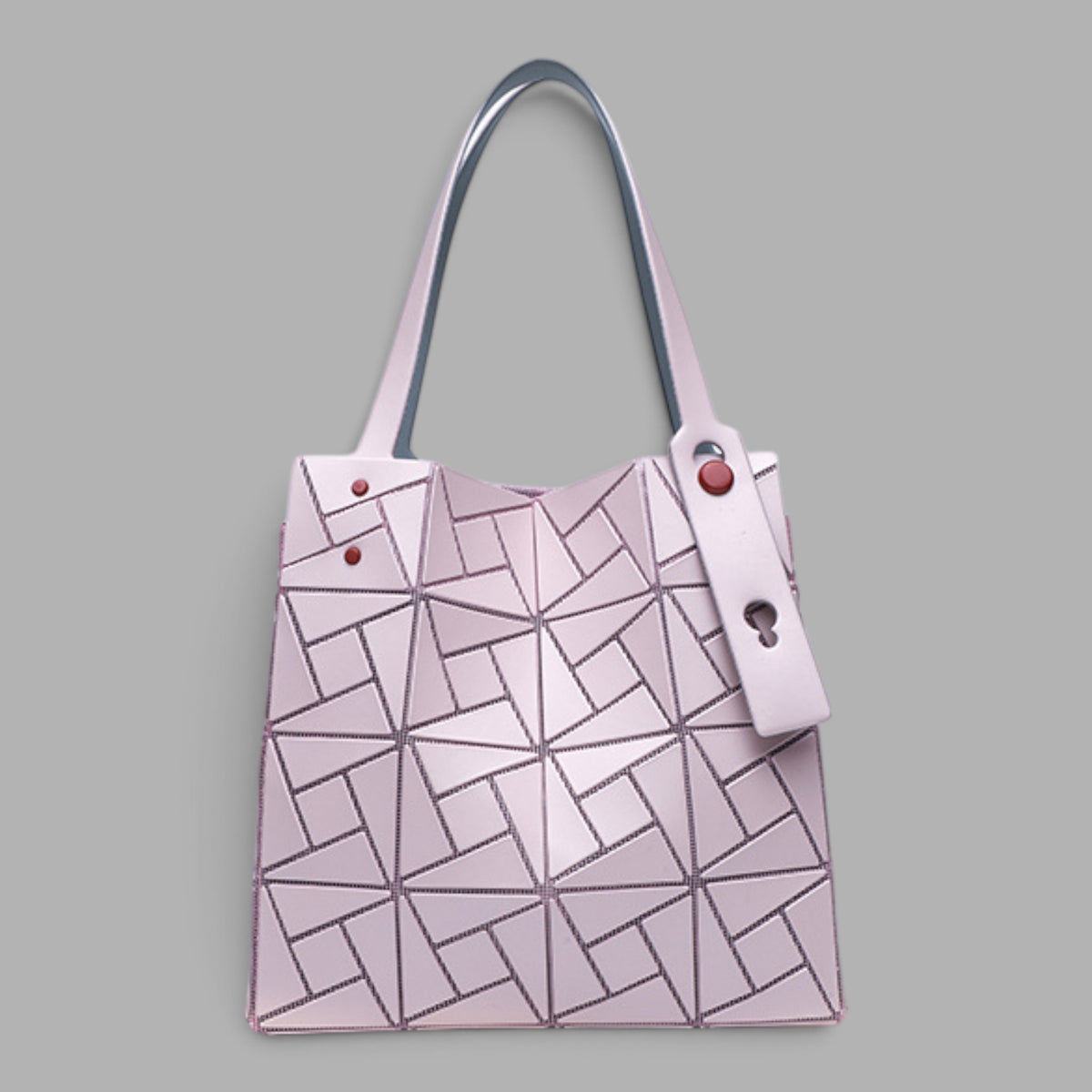 A light pink geometric pleated tote bag with dark gray handles and a matching key ring charm, shown against a solid gray background.