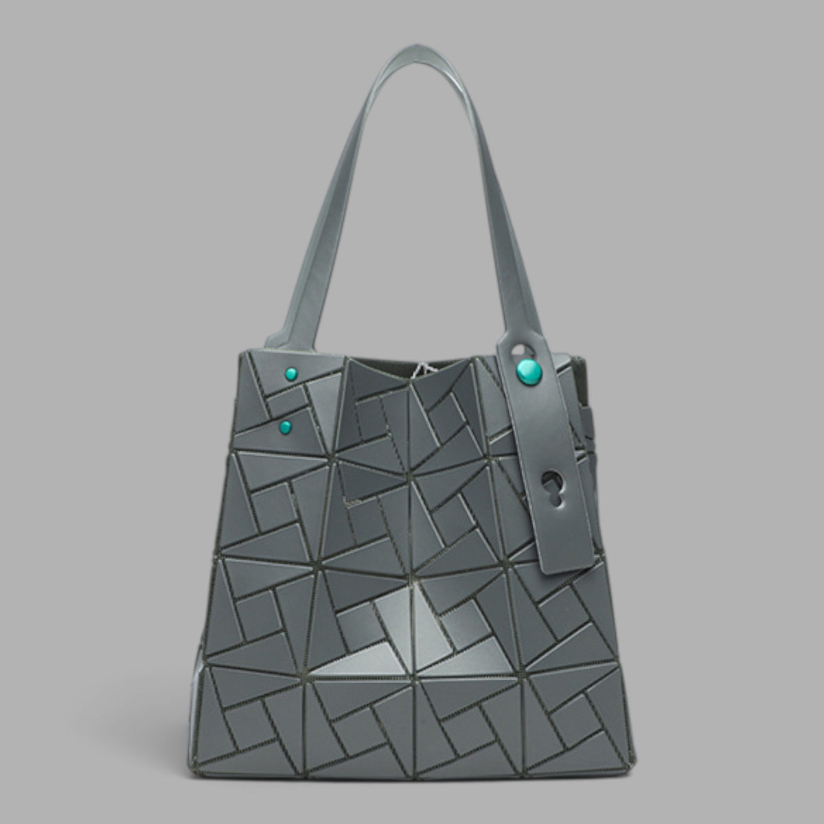 A gray geometric tote bag with a faceted triangular pattern, dual shoulder straps, and small turquoise-colored decorative studs, shown against a solid gray background.