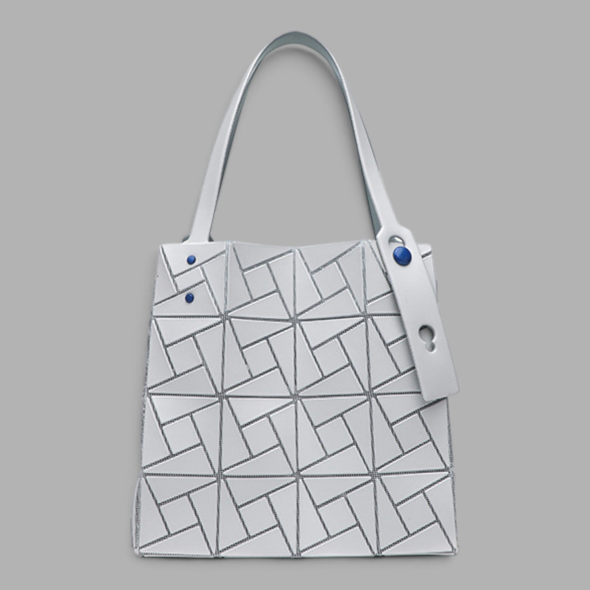 A structured tote bag with a white base and a geometric black line pattern, featuring a matching white shoulder strap and a hanging white tag with blue buttons, set against a solid gray background.
