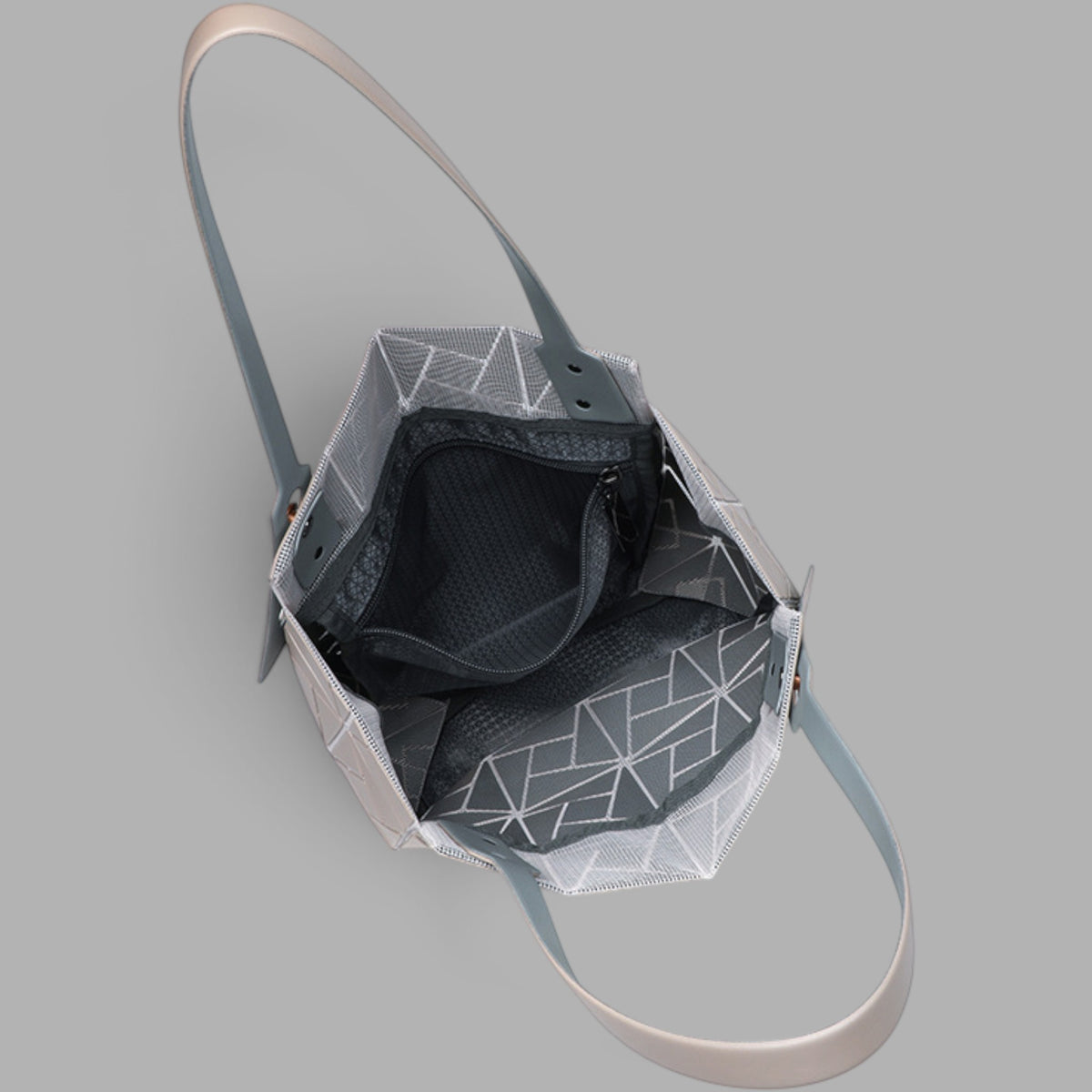 The interior of a structured shoulder bag with a gray and white geometric patterned mesh exterior, a black mesh lining, and a light beige strap, shown on a solid gray background.