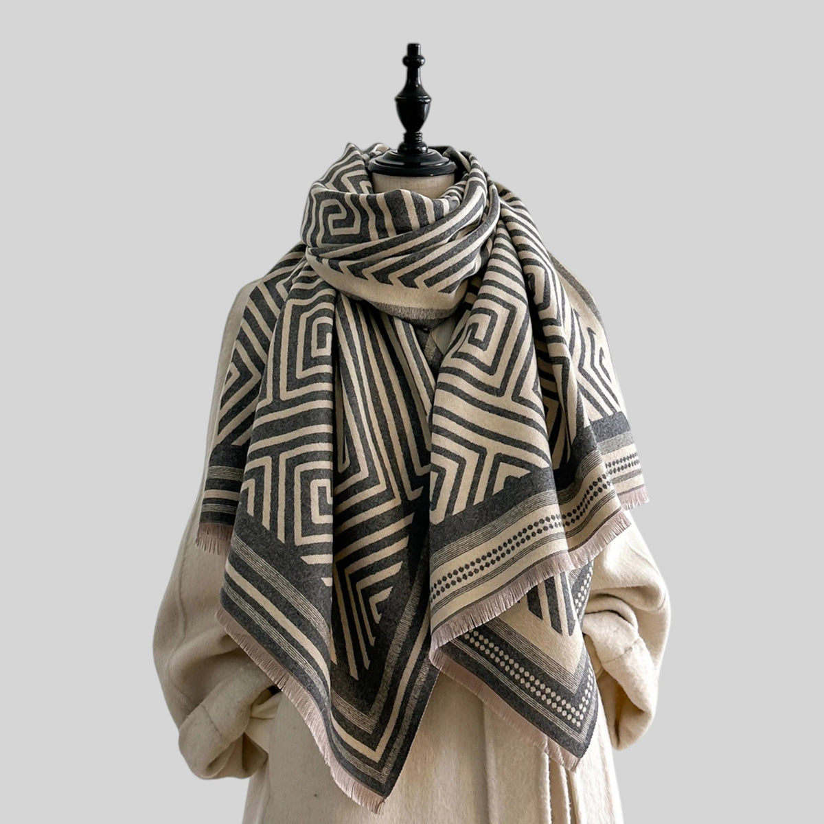 A square white scarf featuring a black geometric pattern of nested concentric rectangles and intersecting lines, with a bold black border, displayed flat against a light gray background.