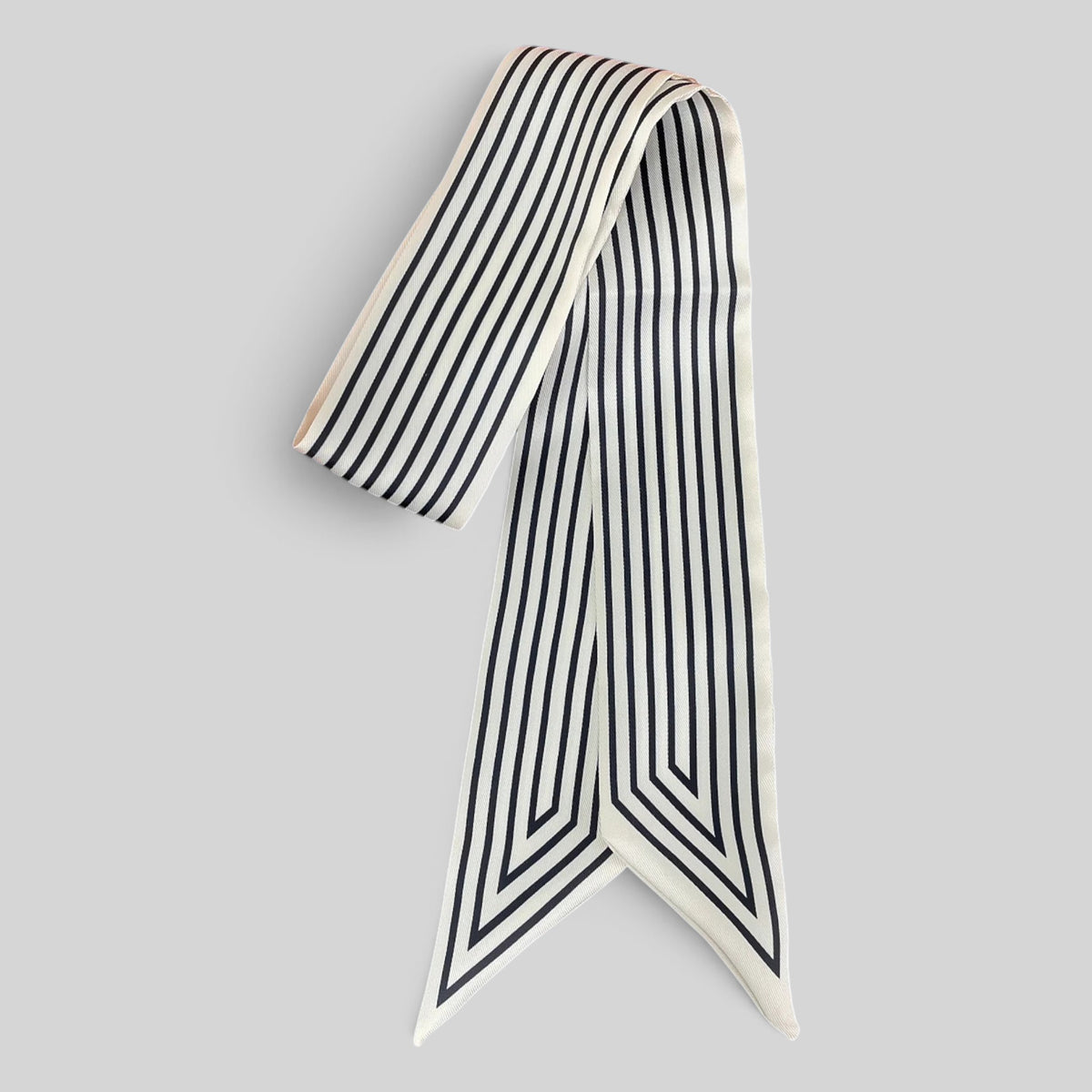 A long narrow scarf with vertical black stripes on an off-white base, arranged in a loop with the ends hanging down, on a solid light gray background.