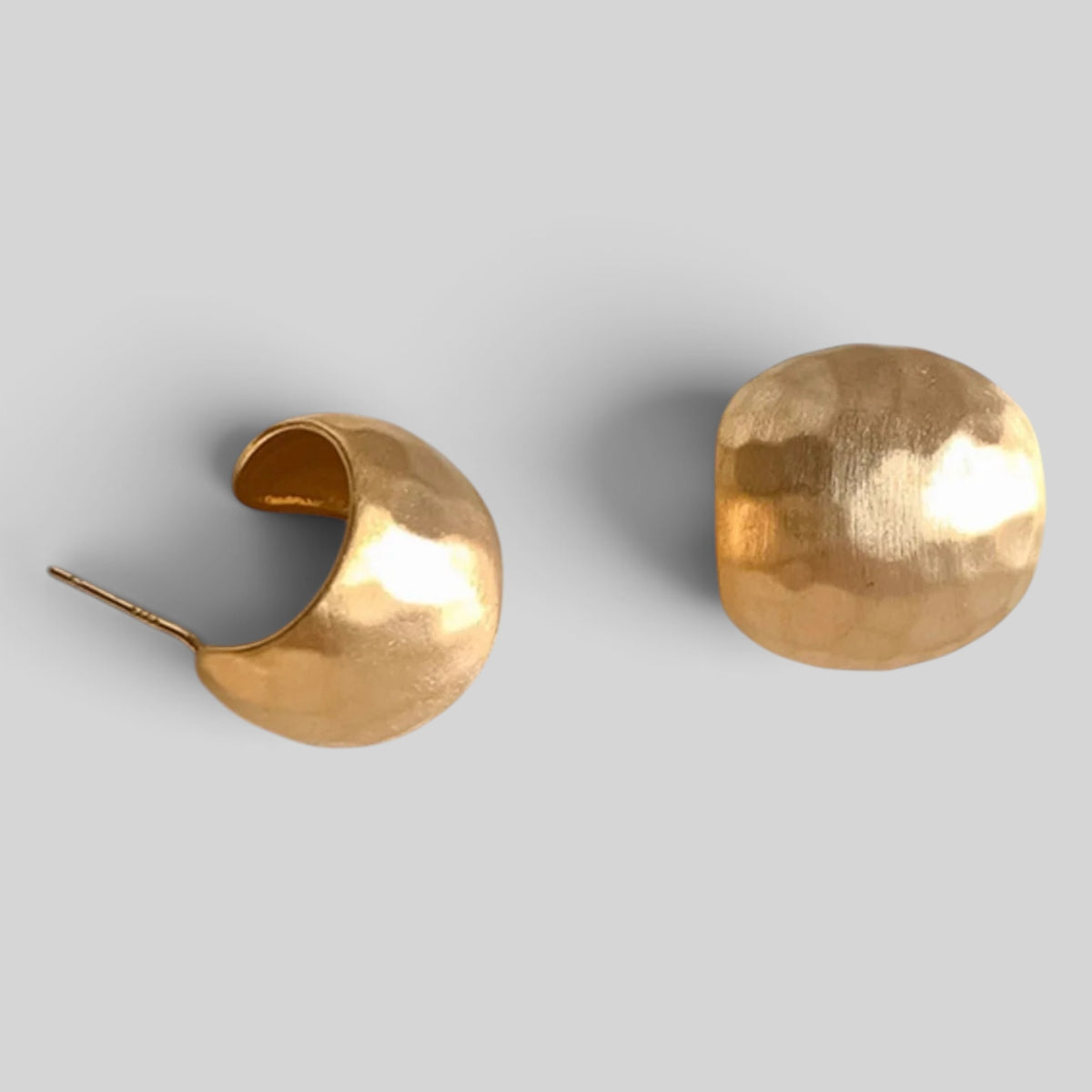 A pair of hammered gold crescent-shaped hoop earrings on a light gray background.
