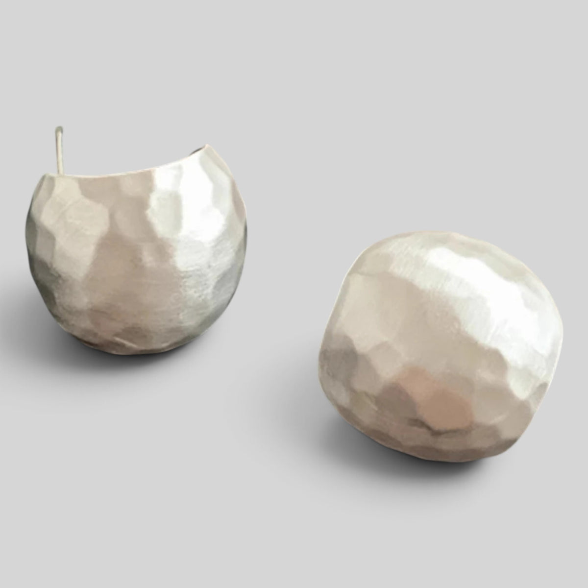 A pair of hammered metallic dome earrings in a silver-tone finish, displayed on a neutral light gray background.