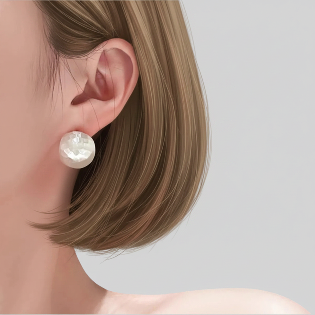 A close-up of a woman's ear wearing a single round pearl stud earring against a soft light gray background.