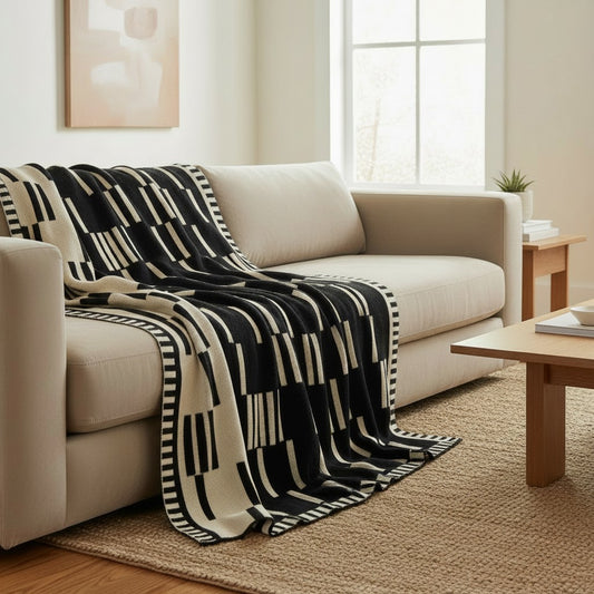 A black and cream geometric patterned throw blanket is draped over a light beige sofa in a bright, modern living room setting.
