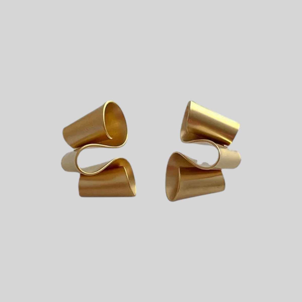 A pair of gold-toned wrap-style earrings with a sculptural, layered spiral design, shown against a solid light gray background.
