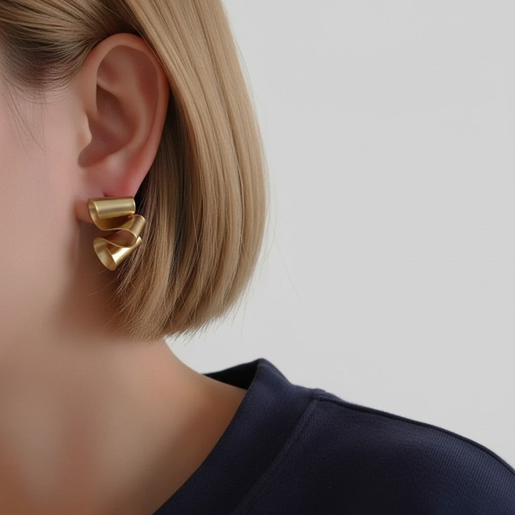 A close-up of a model's ear wearing a sculptural, multi-pronged gold earring against a light gray background.