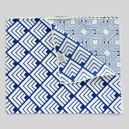 A folded textile product, likely a blanket or throw, featuring a bold blue and white geometric maze-like pattern on a light gray background.