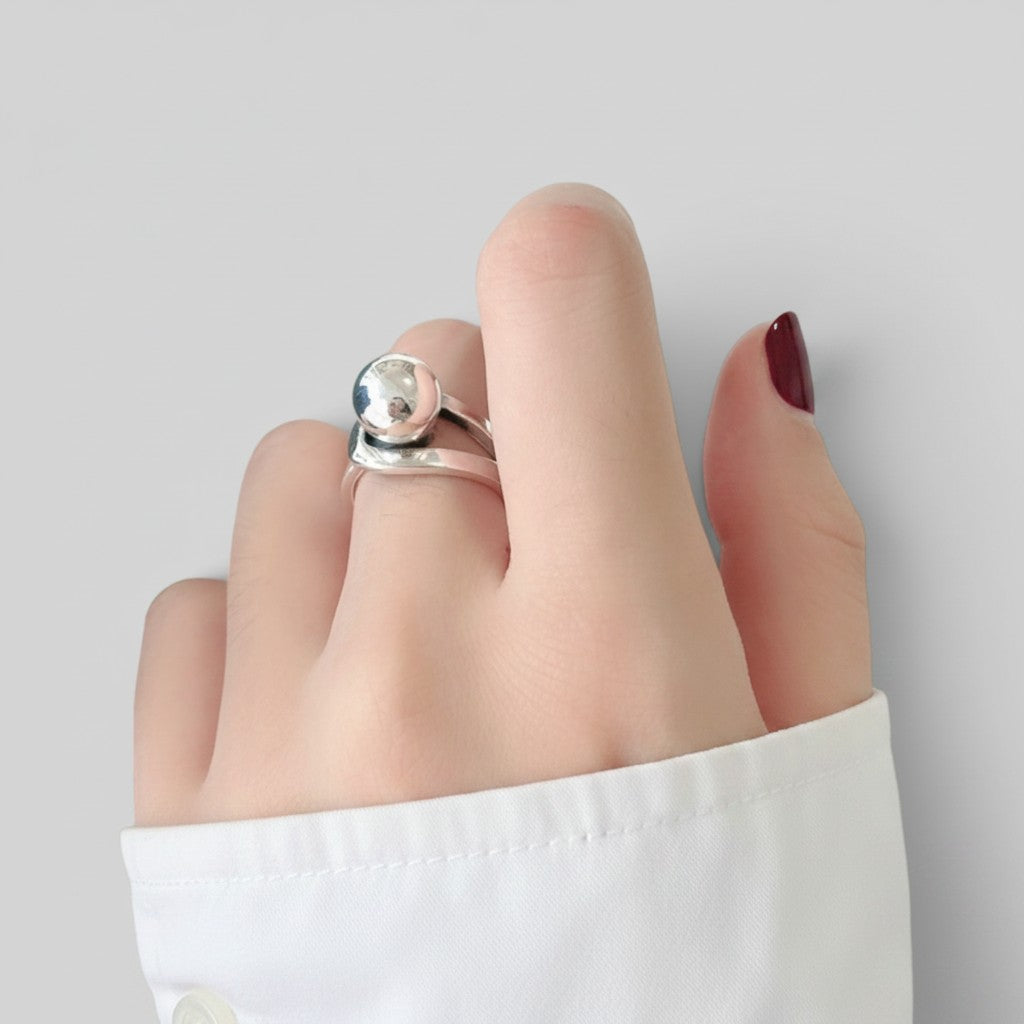 A close-up of a hand wearing a silver ring with a polished oval stone, against a light gray background with a white shirt cuff visible.