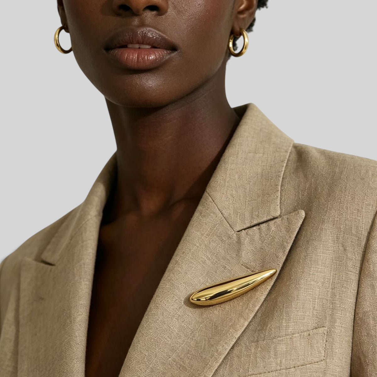 Minimalist gold plated stainless steel oval brooch pin on a beige blazer