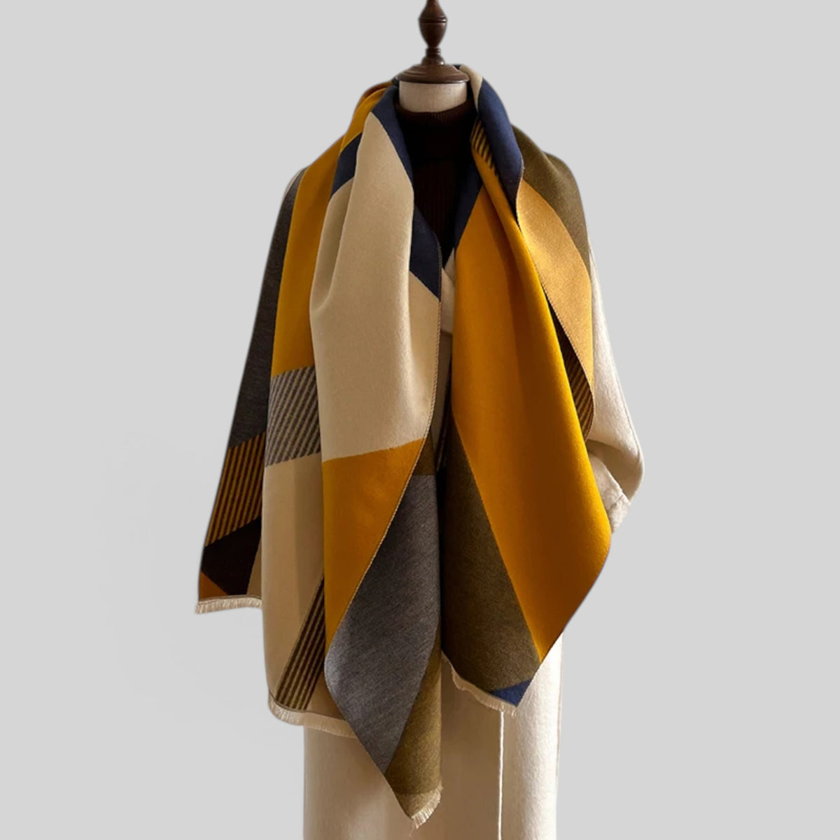 A black and beige striped scarf draped over a gray dress form against a light gray studio background.