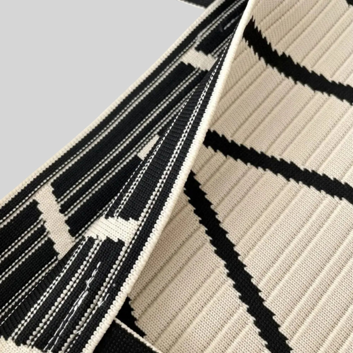 Close-up of a woven textile with a black and off-white geometric pattern, showing the texture and folded edges.