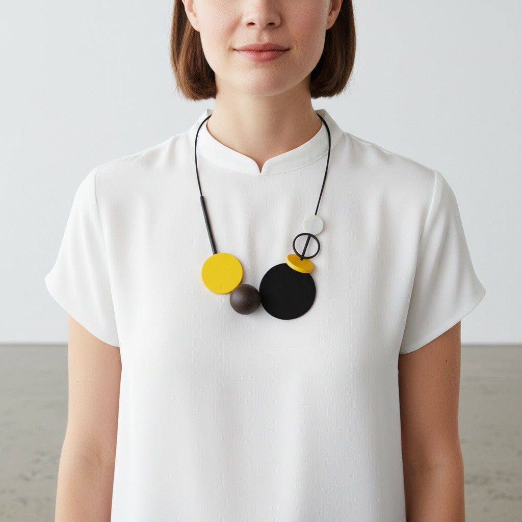 A woman wearing a white short-sleeve top and a modern geometric pendant necklace with black, yellow, and white circular elements.