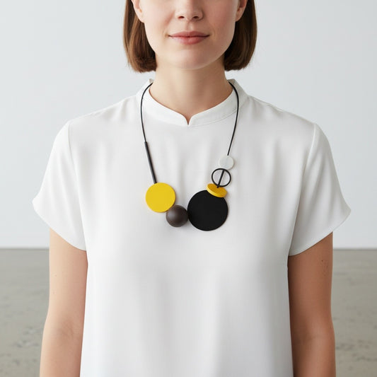 A woman wearing a white short-sleeve top and a modern geometric pendant necklace with black, yellow, and white circular elements.