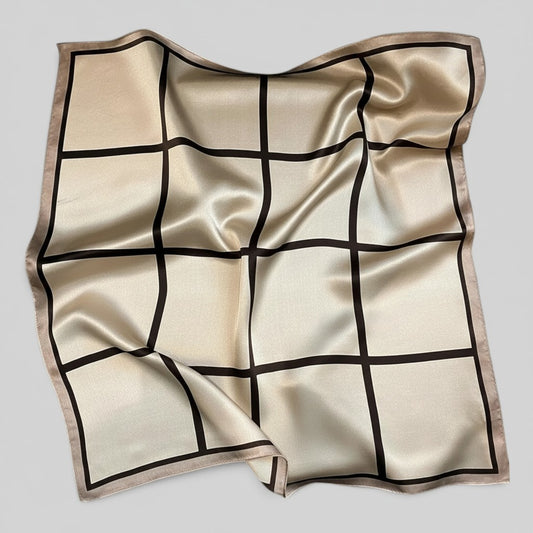 A square silk scarf with a cream and beige base, featuring a black grid pattern and a matching beige border, laid flat on a neutral gray background.