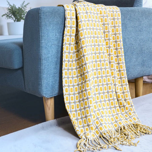 A yellow and gray patterned throw blanket with fringe is draped over the arm of a blue upholstered chair in a living room setting.