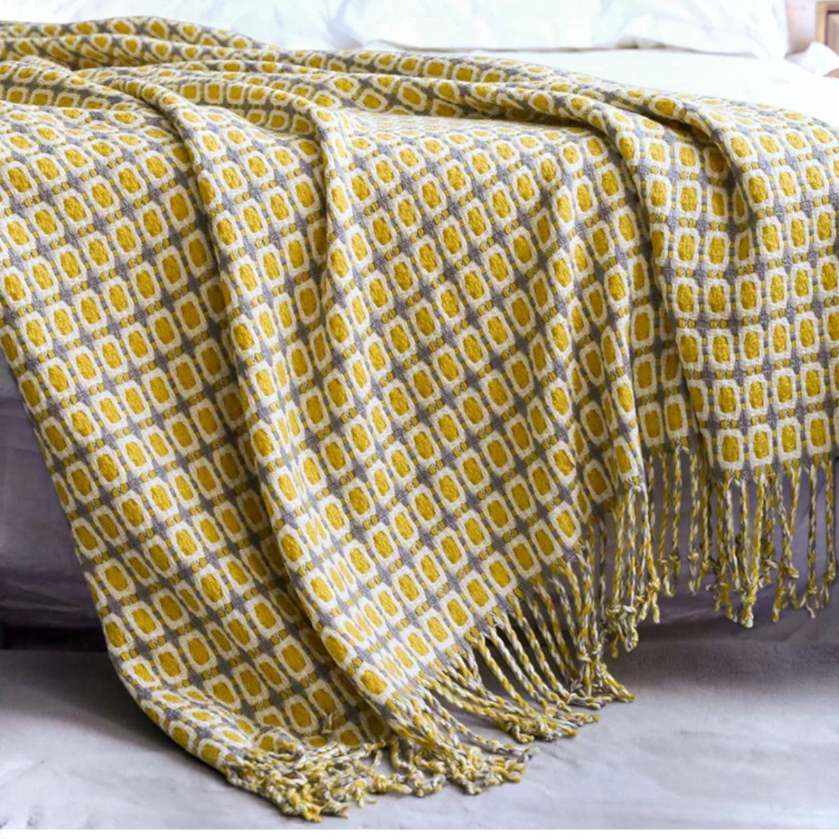 A folded silk scarf with a vibrant geometric color-block pattern, featuring shades of turquoise, royal blue, mustard yellow, burgundy, and cream on a light gray background.