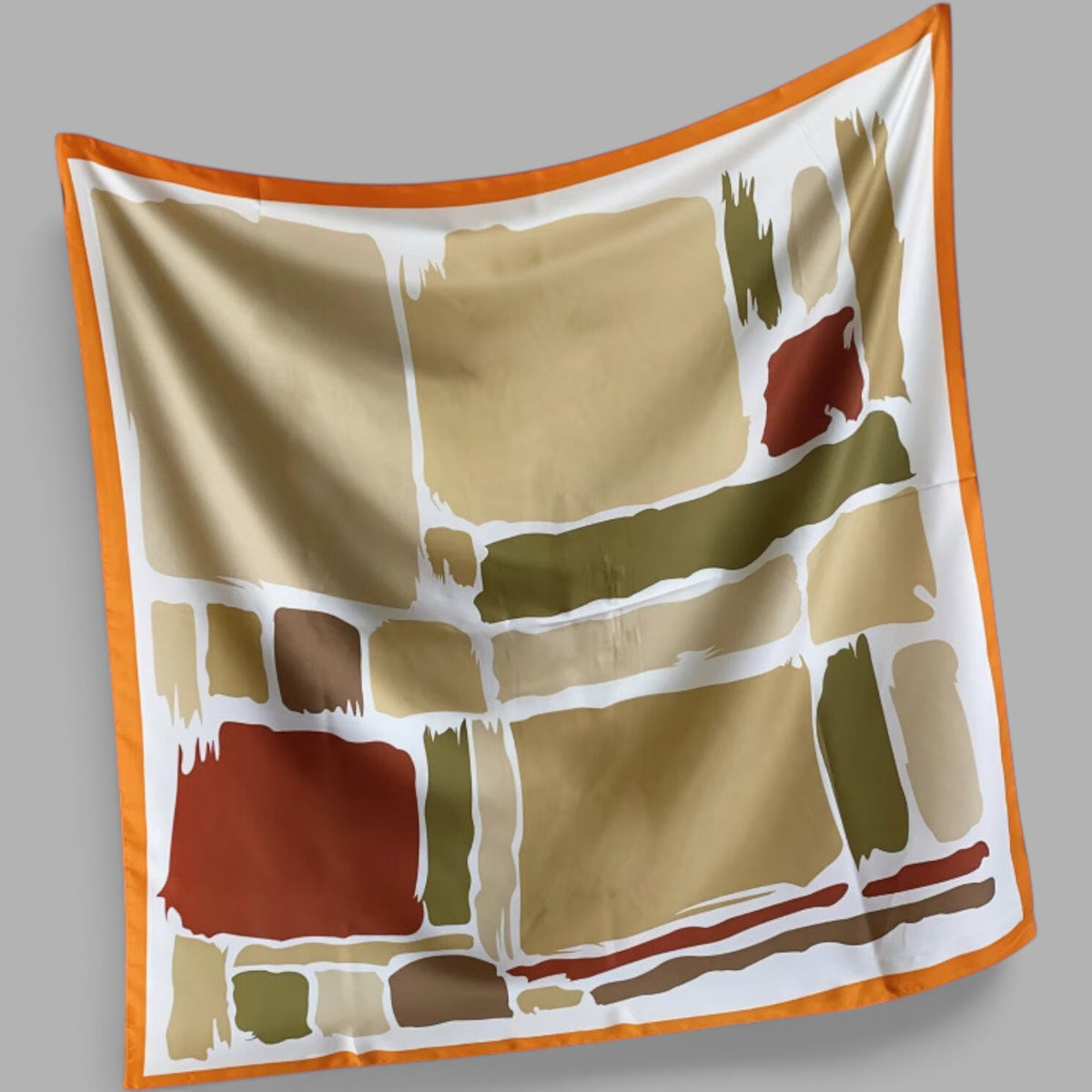 A close-up of a satin scarf with a bold abstract geometric pattern in pink, green, white, orange, and burgundy, finished with a cream border, draped on a light gray background.