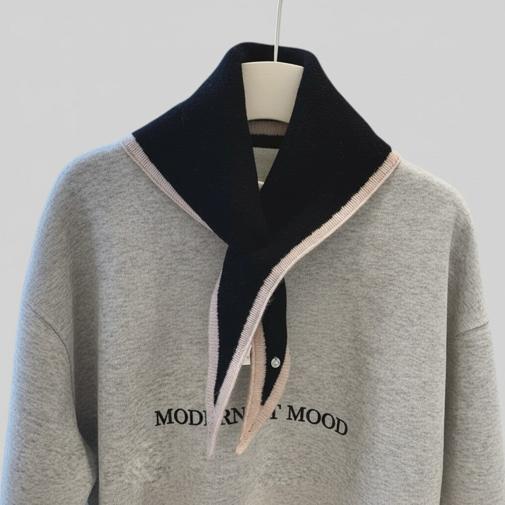 A light gray knit sweater with a large black collar trimmed in pale pink, featuring the words 'MODERNIST MOOD' printed in black across the chest, displayed on a hanger against a light gray background.