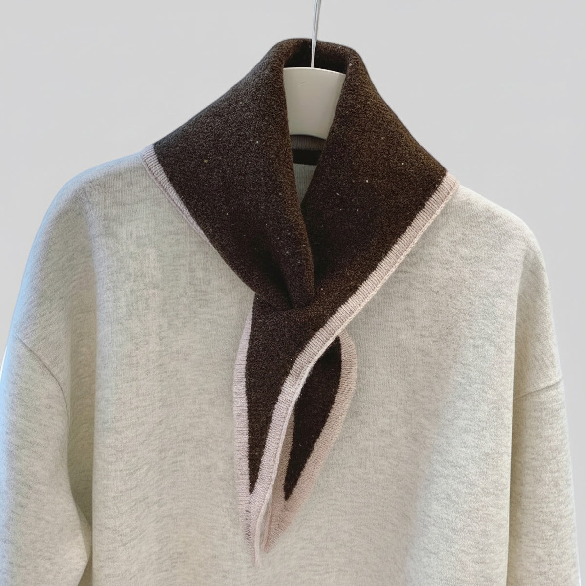 A light heather gray knit sweater with a wide, structured dark brown collar featuring a contrasting pale blush pink inner lining and trim, displayed on a white hanger against a light gray background.