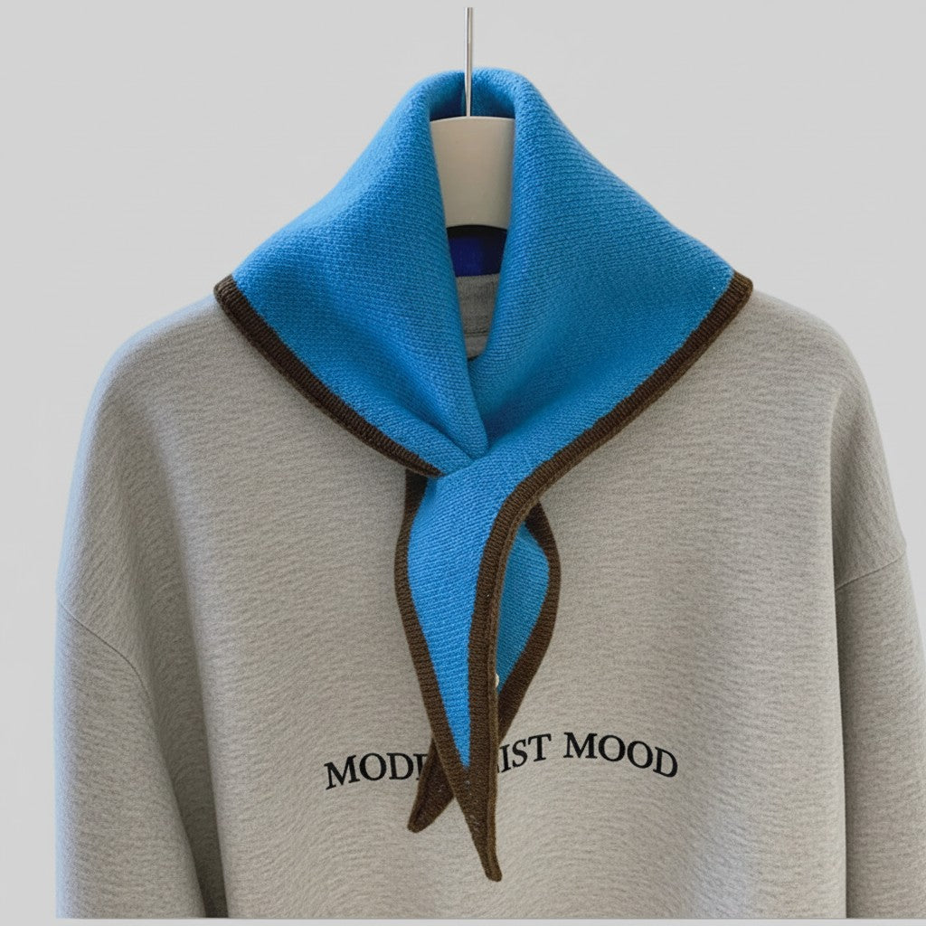A bright blue knit scarf with dark brown trim draped over the collar of a light gray sweatshirt on a mannequin. The sweatshirt has black text reading 'MODERNIST MOOD'.