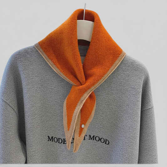 A gray knit sweater with a large orange collar and a matching orange scarf draped around the neck, displayed on a hanger against a light gray background.