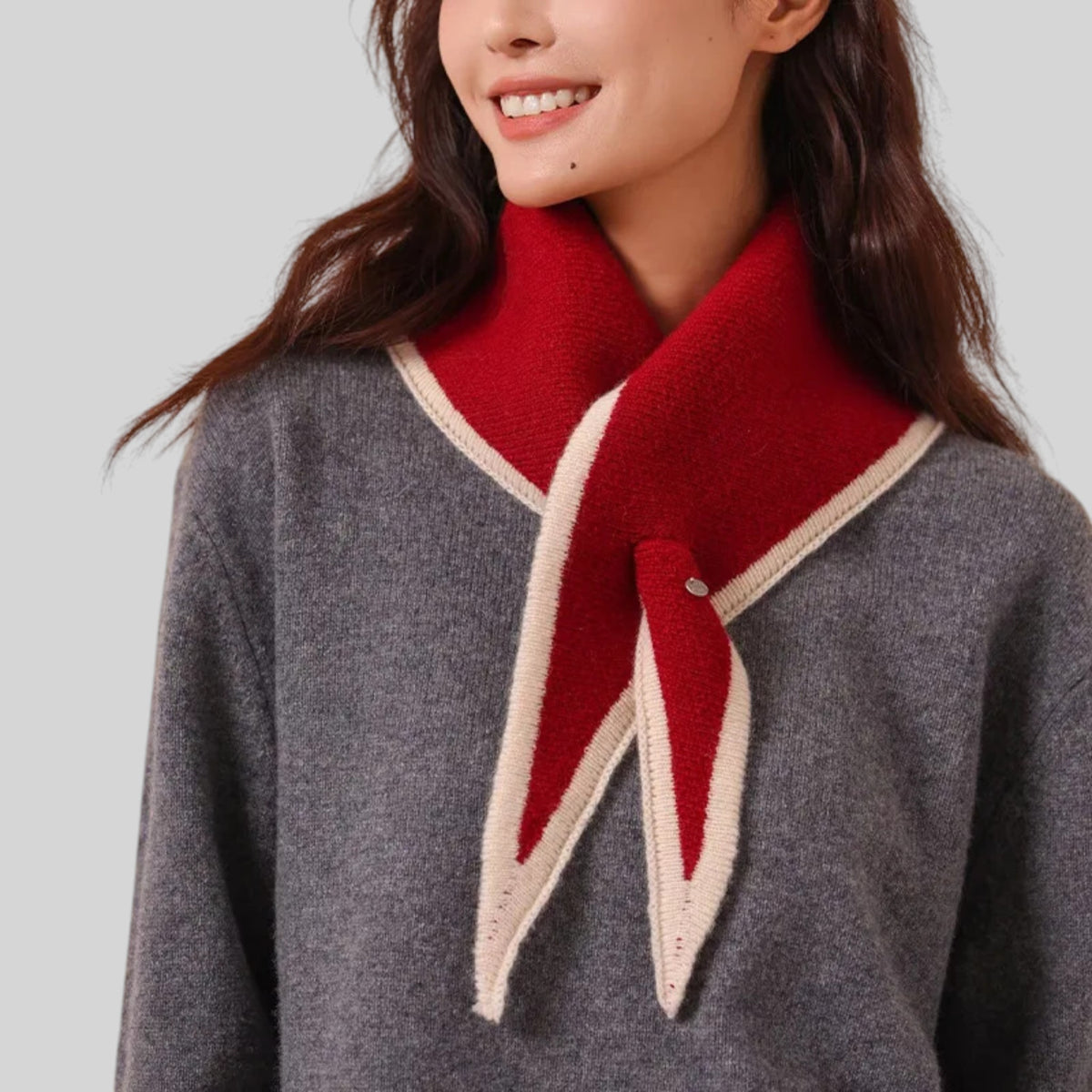 A close-up of a woman wearing a gray knit sweater with a bold red and cream knit collar detail, shown against a light gray background.