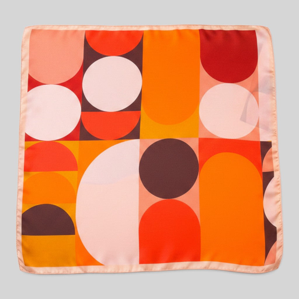 A square silk scarf featuring a mid-century modern geometric pattern with orange, red, pink, and white shapes, displayed flat against a neutral gray background.