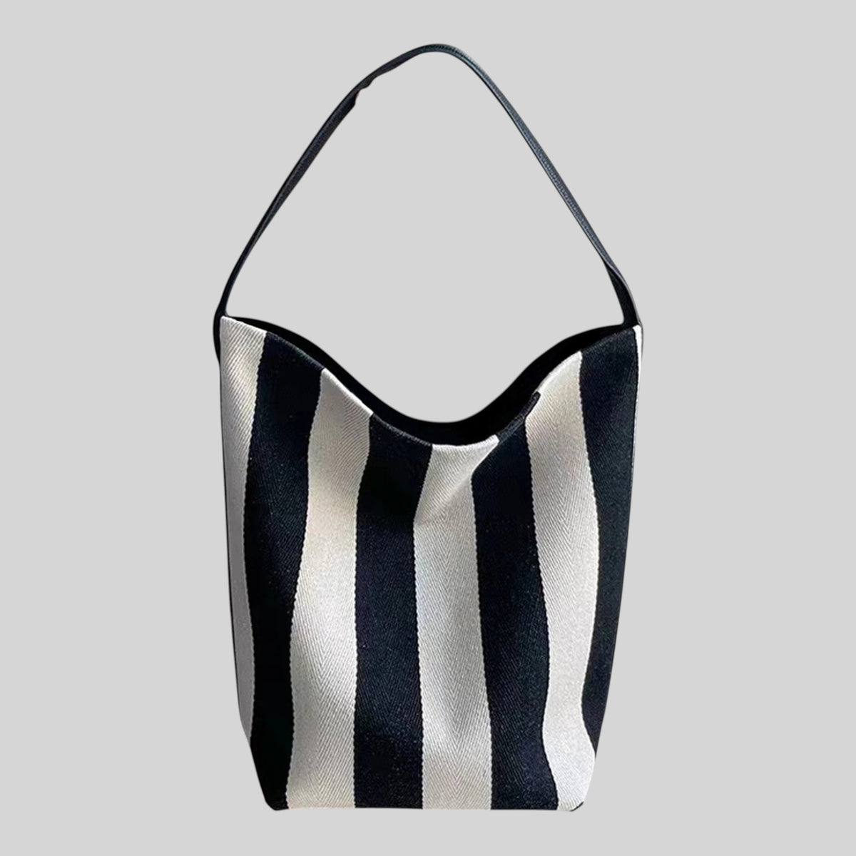 A black and white vertically striped shoulder bag with a single black strap, shown against a solid light gray background.
