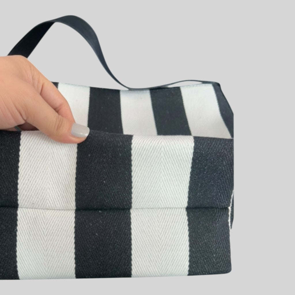 A close-up of a hand holding a black and white striped fabric bag or pouch against a plain light gray background.
